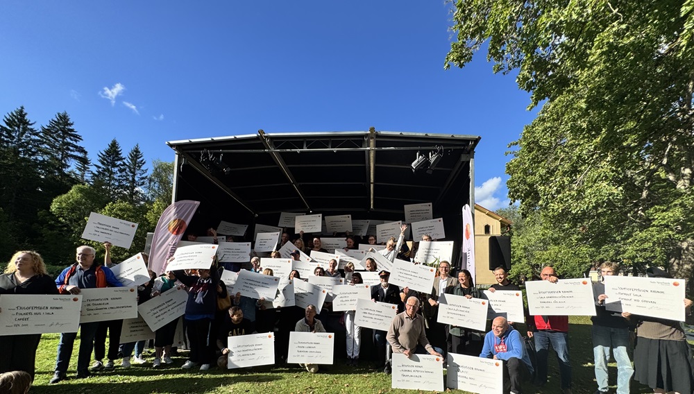 En stor grupp med människor står på och runt om en scen och håller upp checkar som de mottagit i utdelningen av Miljonen.